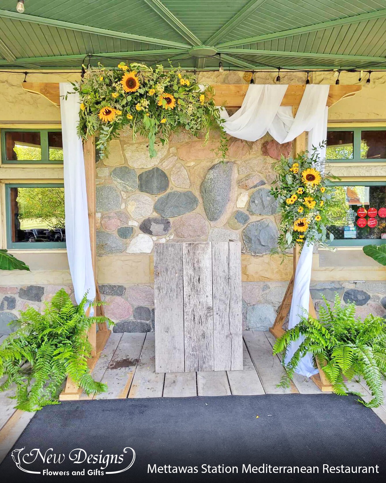 An square arch draped with white material, greenery and sunflowers sits under the rustic patio of Mettawas Train Station and Mediterranean Restaraunt in Kingsville.